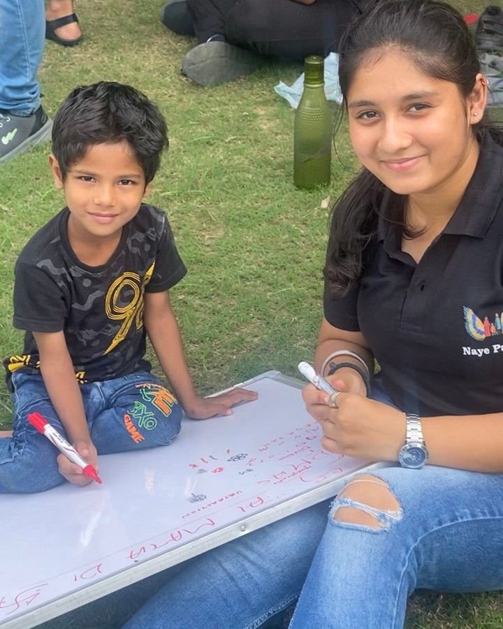A smiling NayePankh volunteer learning with a happy child outdoors