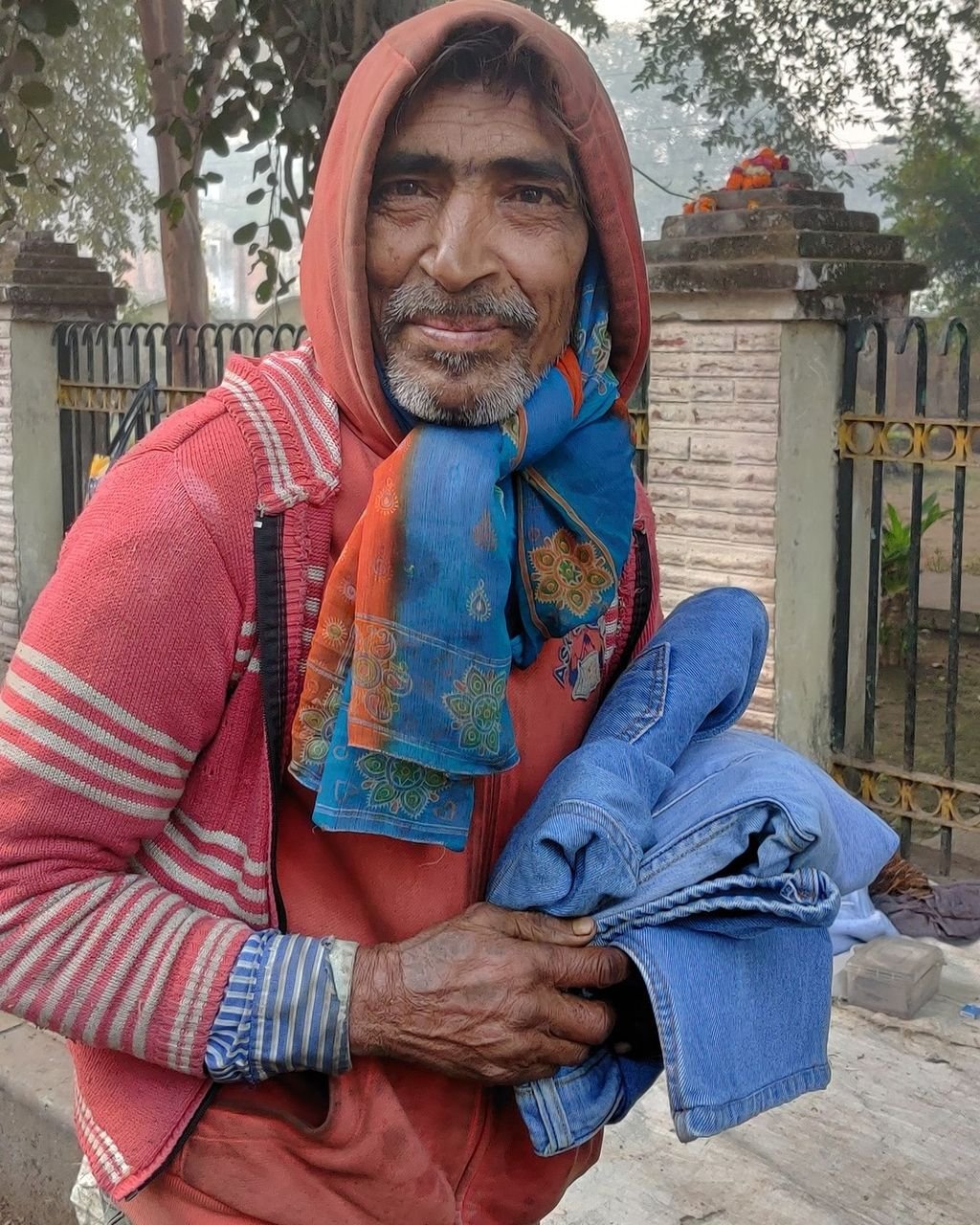 A dignified elder holding warm clothes from a distribution drive